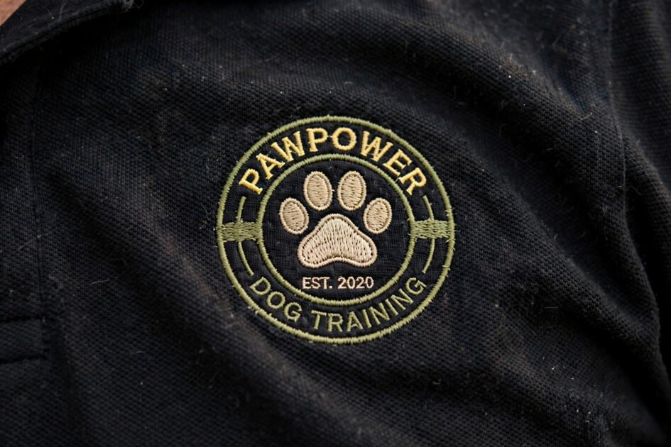 Close-up of an embroidered paw print logo on the chest of a black dog trainer polo shirt